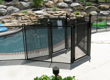 Black mesh pool fence and gate around a pool with a stone-wall garden