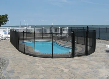 Black mesh pool fence around a freeform pool beside the bay