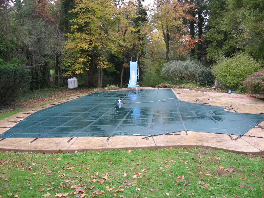 Green Loop-Loc mesh safety cover installed over an inground pool for winter